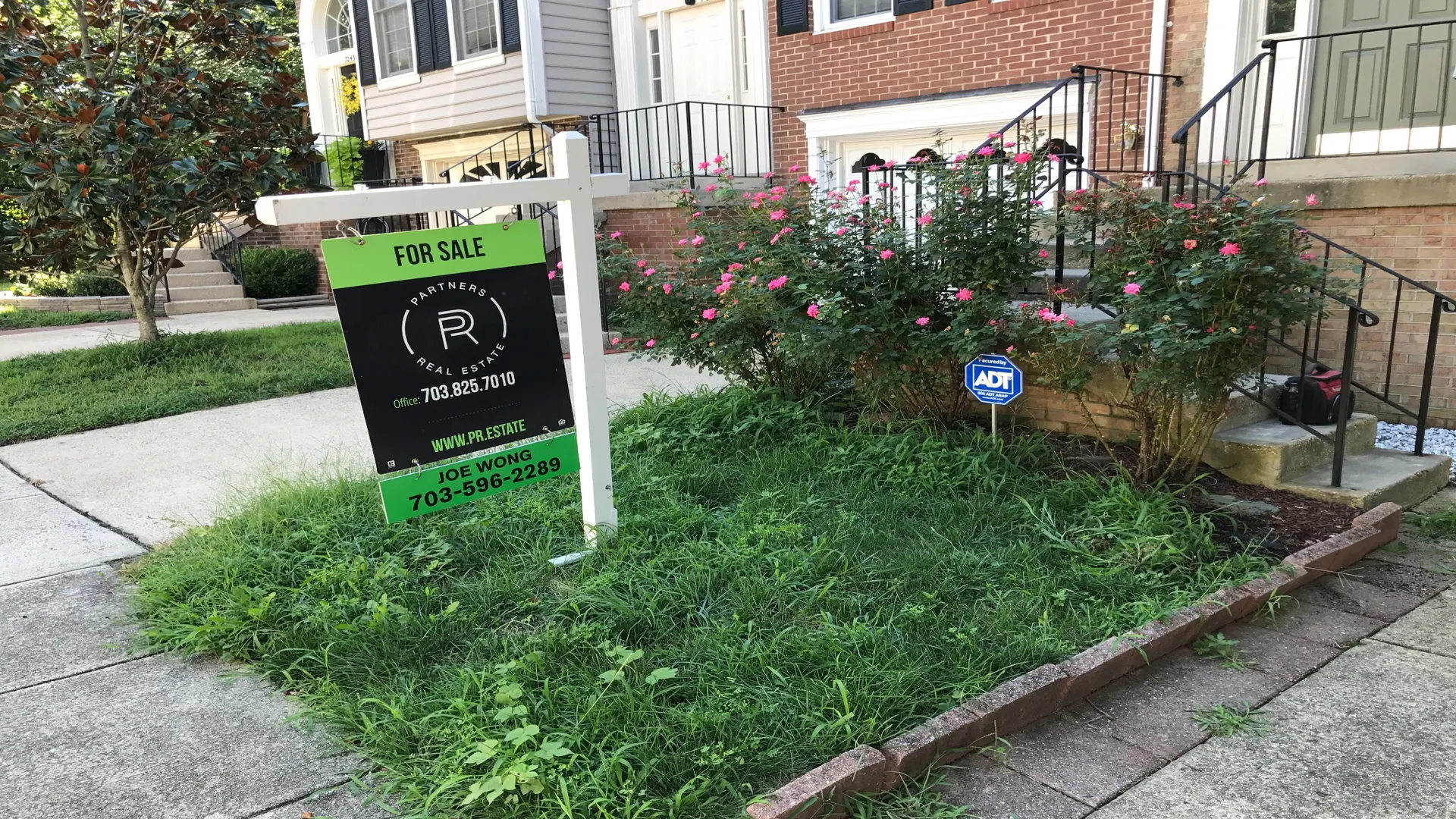 Townhouse front yard with overgrown bushes and weeds.